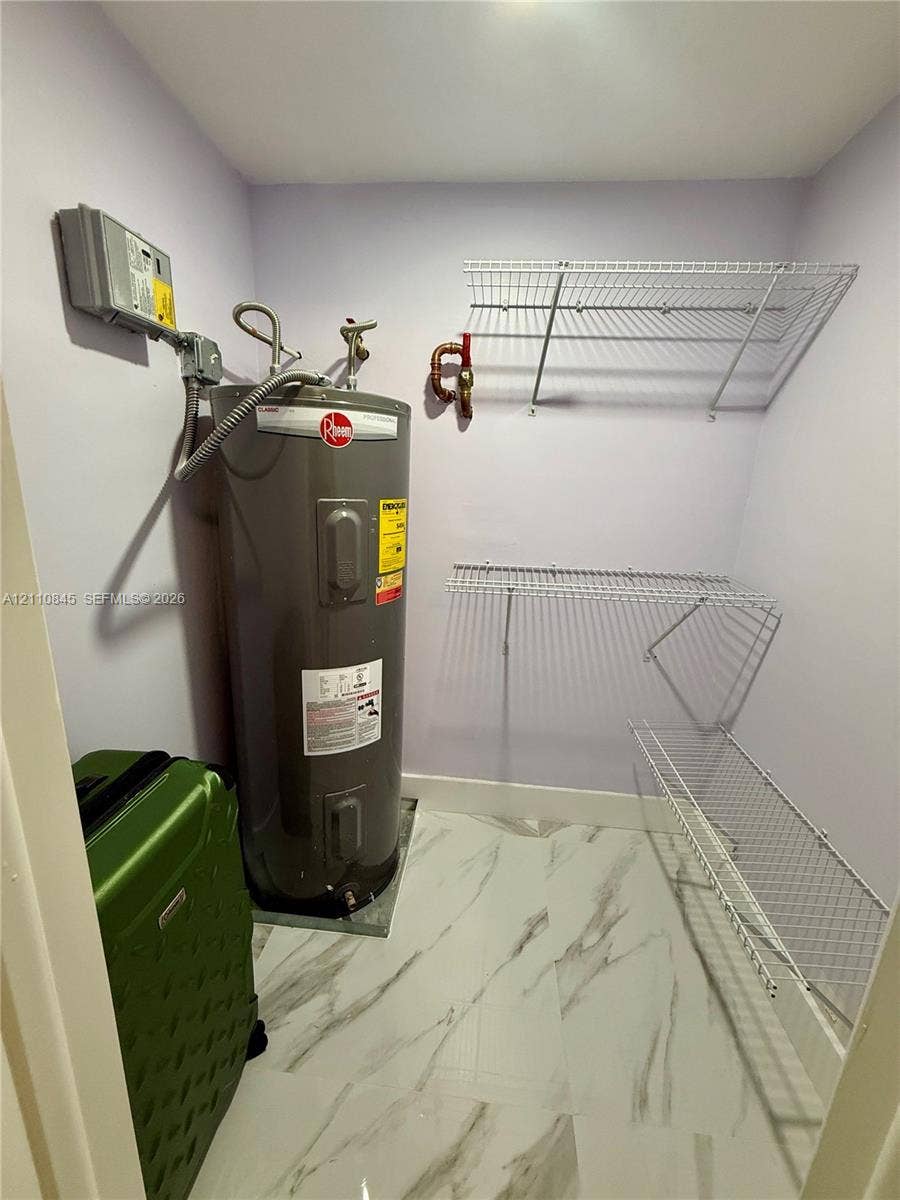 565 Oaks Lane, #410, Pompano Beach, FL 33069 Utility space featuring large-format tile flooring, a Rheem water heater, and wall-mounted wire shelving