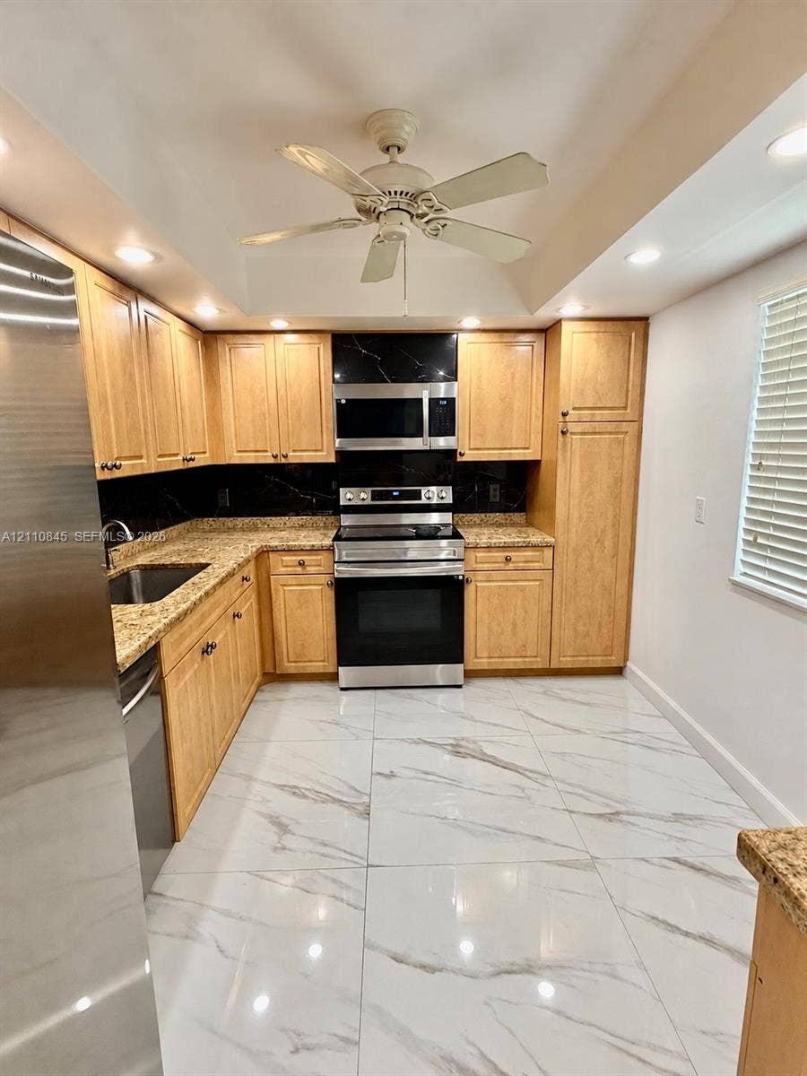 565 Oaks Lane, #410, Pompano Beach, FL 33069 Kitchen featuring light wood cabinetry, stone countertops, stainless steel appliances, a dark stone backsplash, and large-format tile flooring