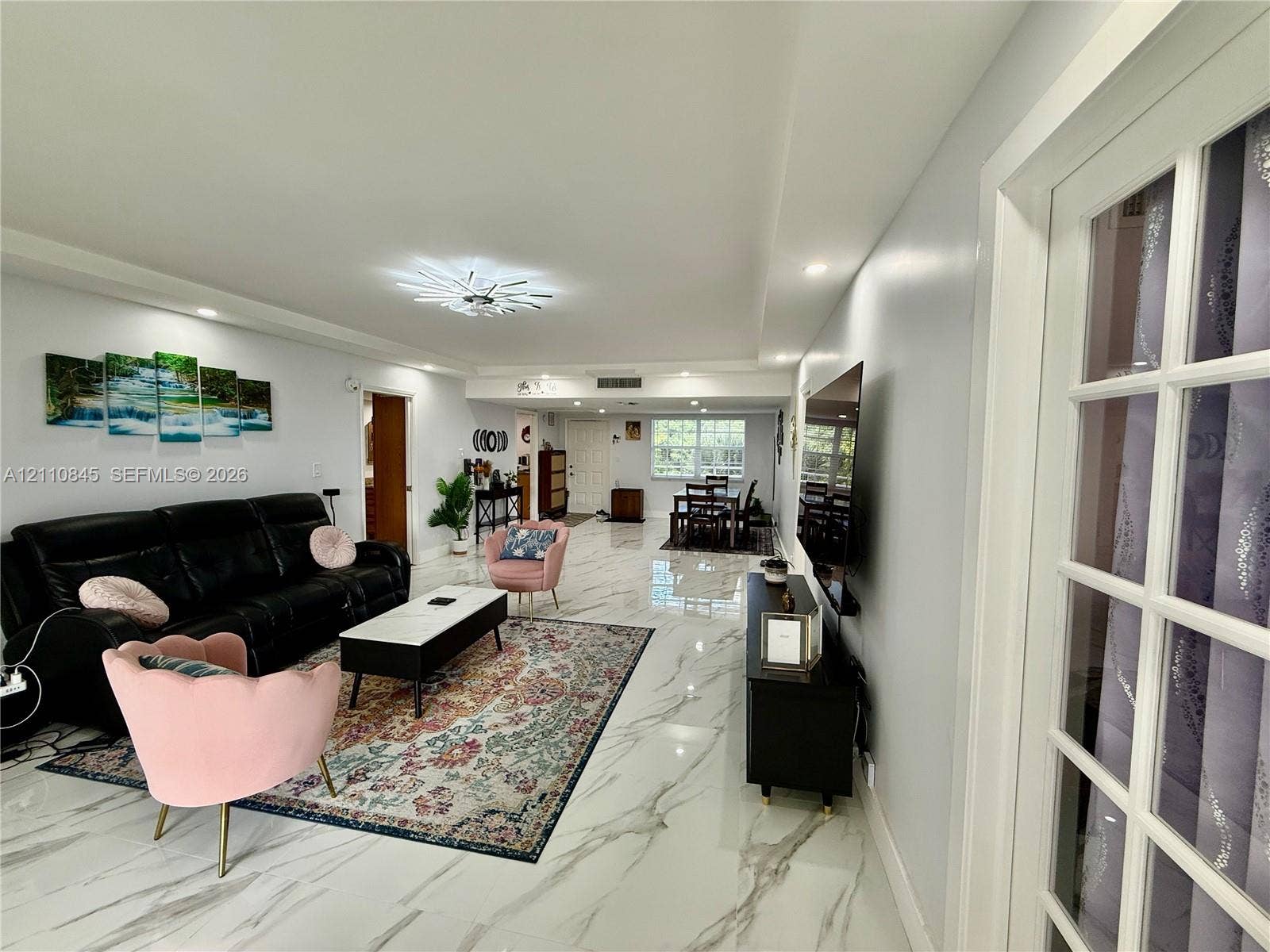 565 Oaks Lane, #410, Pompano Beach, FL 33069 Open-concept living space featuring large-format tile flooring with vein detailing, recessed ceiling lighting, a multi-arm modern light fixture, and white French doors