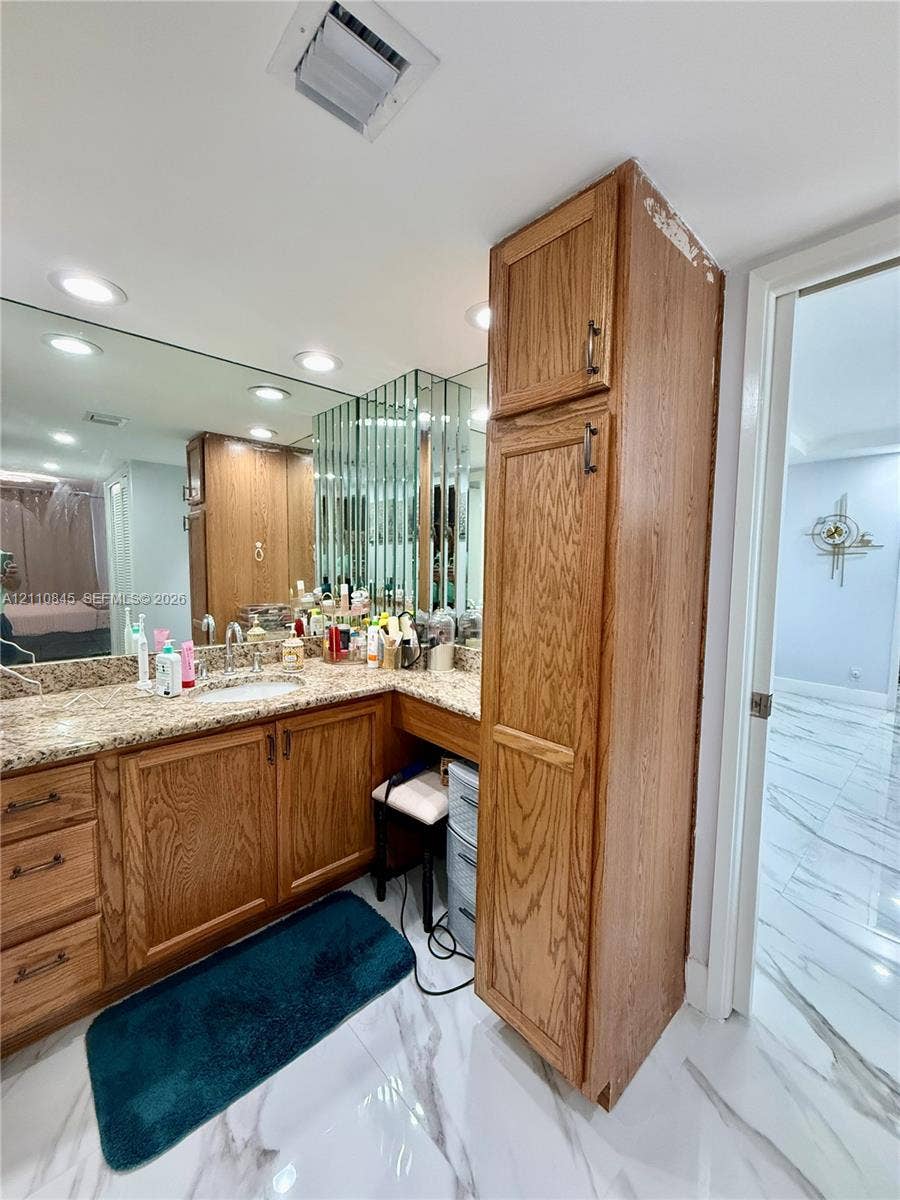 565 Oaks Lane, #410, Pompano Beach, FL 33069 Vanity featuring wood cabinetry, natural stone countertop, recessed lighting, integrated full-wall mirror, and floor-to-ceiling storage cabinet