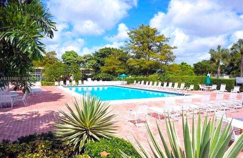 565 Oaks Lane, #410, Pompano Beach, FL 33069 Swimming pool featuring a brick-paved deck, tropical landscaping, and mature foliage