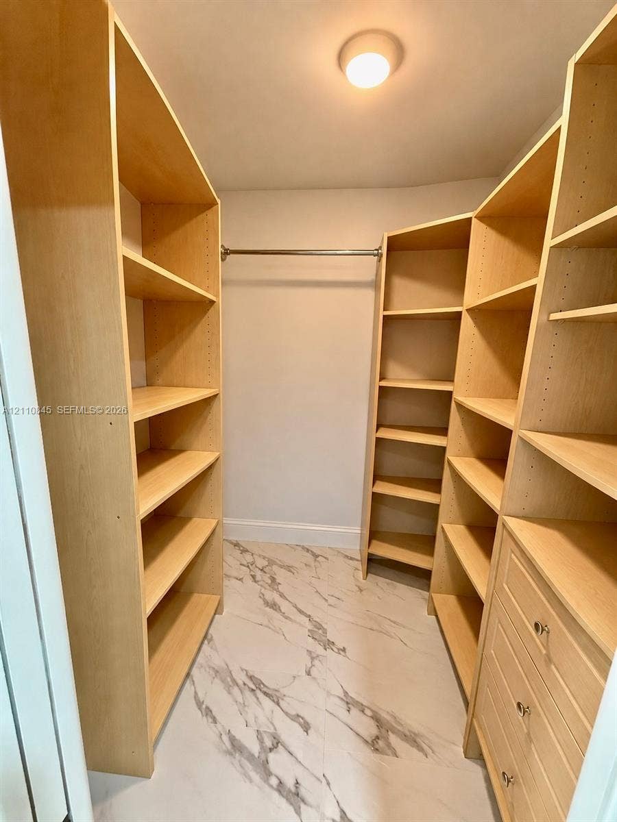 565 Oaks Lane, #410, Pompano Beach, FL 33069 Walk-in closet featuring light-toned custom shelving, integrated drawer stack, metal hanging rod, and large-format tile flooring with a marble-patterned finish