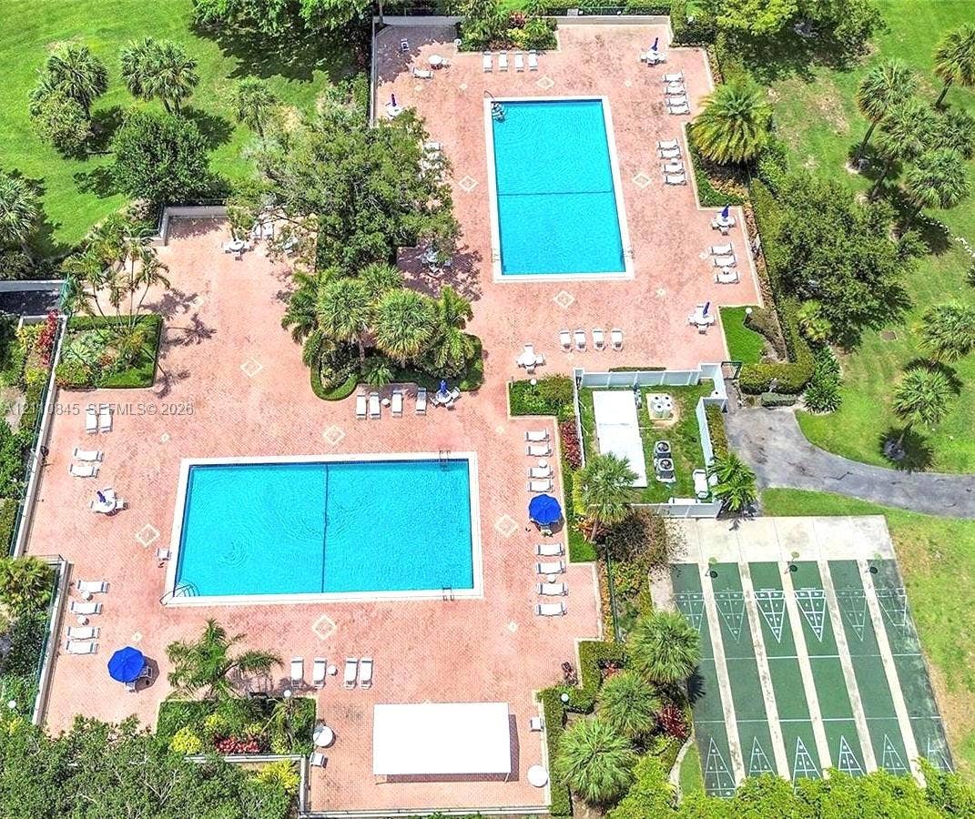 565 Oaks Lane, #410, Pompano Beach, FL 33069 Recreational area featuring two rectangular swimming pools, expansive paved sun deck, and multiple shuffleboard courts surrounded by mature landscaping