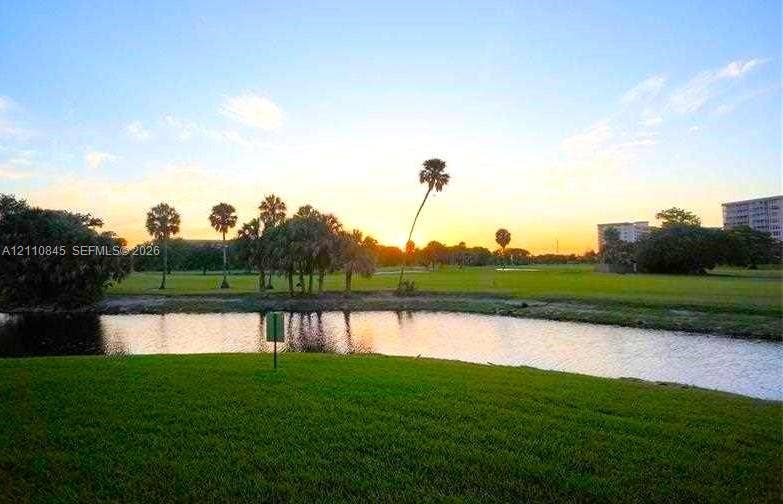 565 Oaks Lane, #410, Pompano Beach, FL 33069 Waterfront lot featuring a manicured lawn, established palm trees, and an open grass expanse