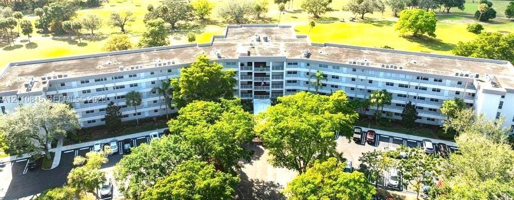 565 Oaks Lane, #410, Pompano Beach, FL 33069 Multi-story residential building featuring private balconies, expansive grounds with mature trees, and surface parking