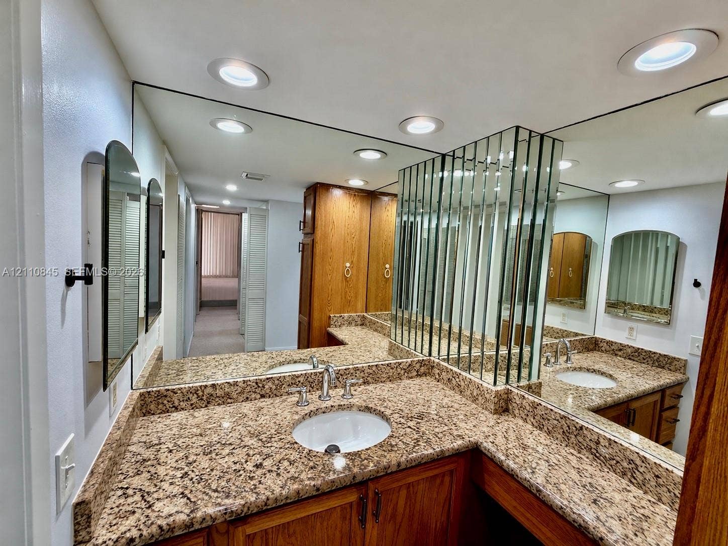565 Oaks Lane, #410, Pompano Beach, FL 33069 Stone-surface countertop with integrated oval basin, natural wood-finish cabinetry, floor-to-ceiling mirror paneling, and recessed ceiling lighting