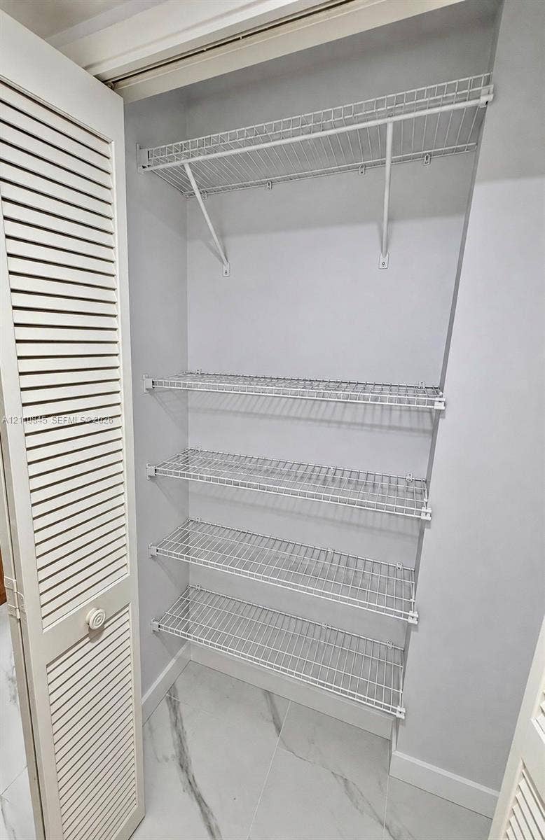 565 Oaks Lane, #410, Pompano Beach, FL 33069 Storage area featuring louvered bi-fold doors, four-tier ventilated wire shelving, and stone-finish flooring