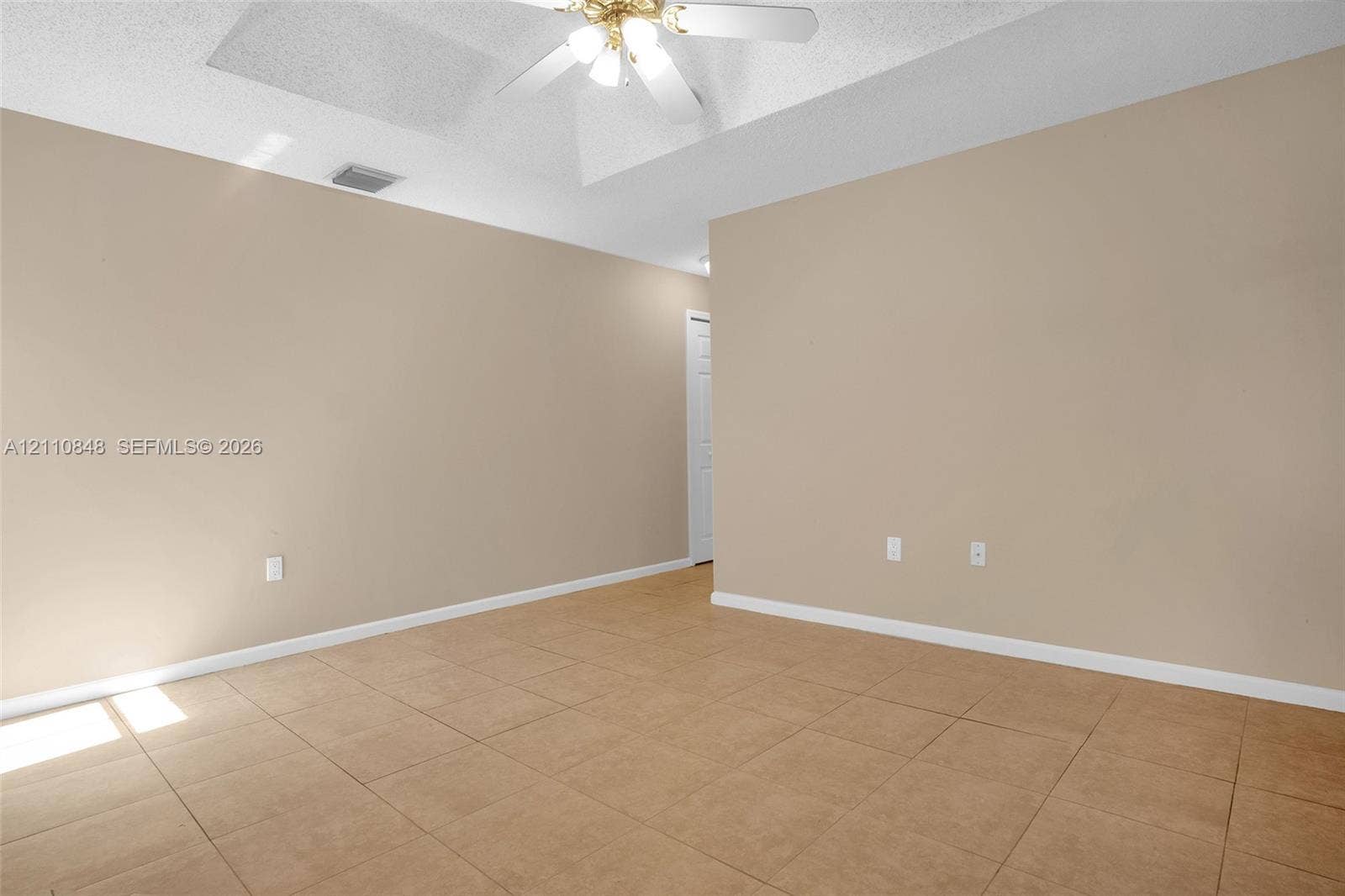 Neutral-toned interior space featuring tile flooring, a tray ceiling, and a ceiling fan with integrated light fixture