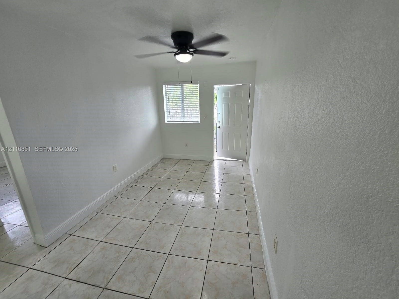 Neutral-toned tiled flooring, white walls, integrated ceiling fan with light fixture, and horizontal blinds