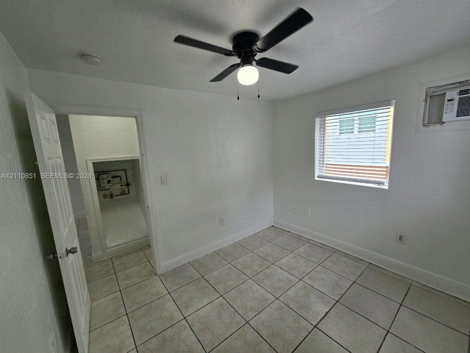 Neutral-toned tile flooring, white wall finish, ceiling fan with integrated lighting, and a multi-pane window with blinds
