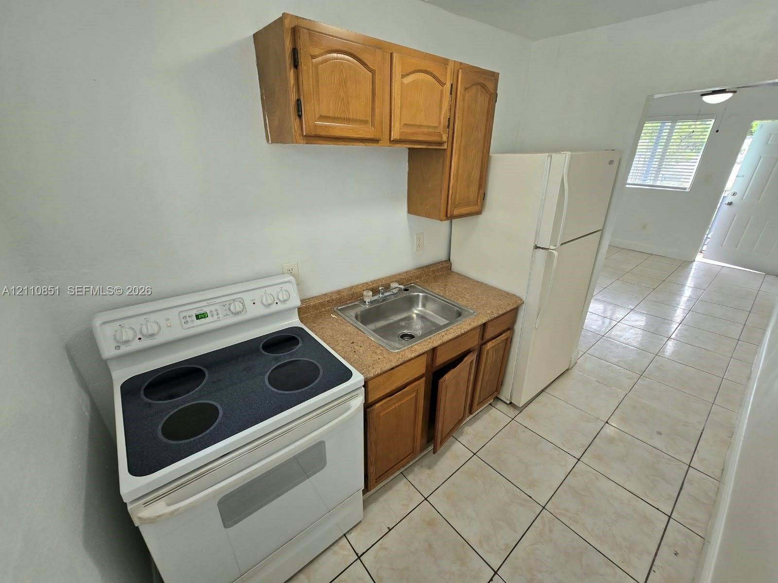 Kitchen area featuring wood cabinetry, solid-surface countertops, a stainless steel sink, an electric range, and tile flooring