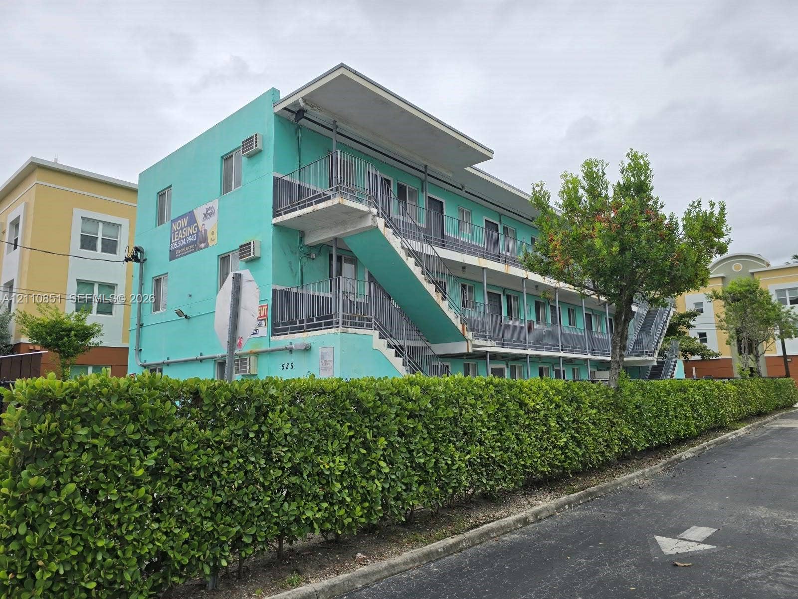 Three-story exterior featuring a flat roofline, metal exterior staircases, railed balconies, and a manicured hedge perimeter
