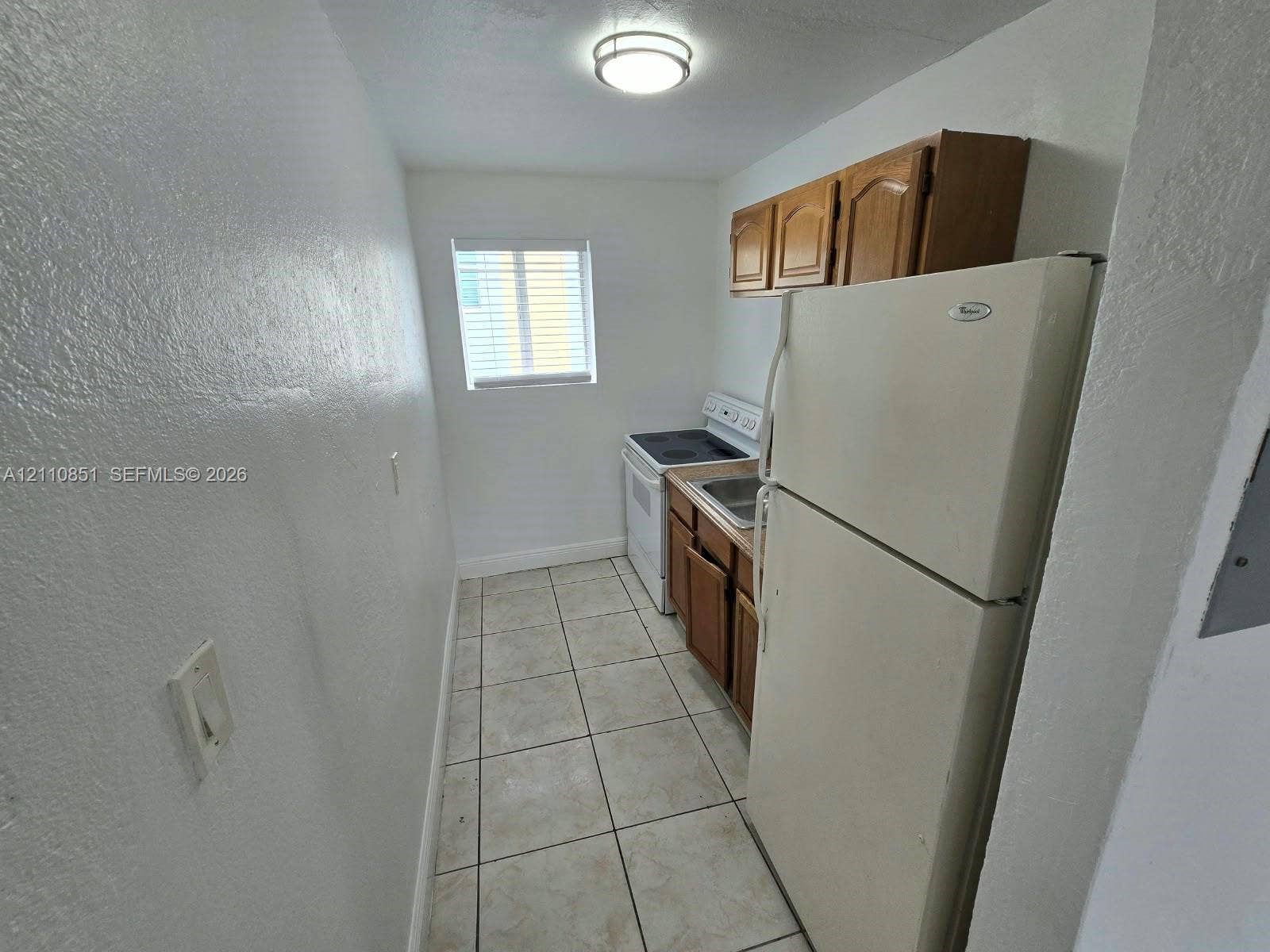 Kitchen featuring tile flooring, wood-finish cabinetry, a white refrigerator, and an electric range