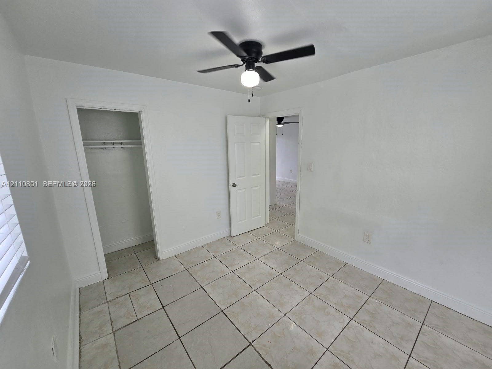 Room featuring light-toned tile flooring, a matte black ceiling fan with an integrated light fixture, a six-panel interior door, and a built-in closet with an overhead shelf