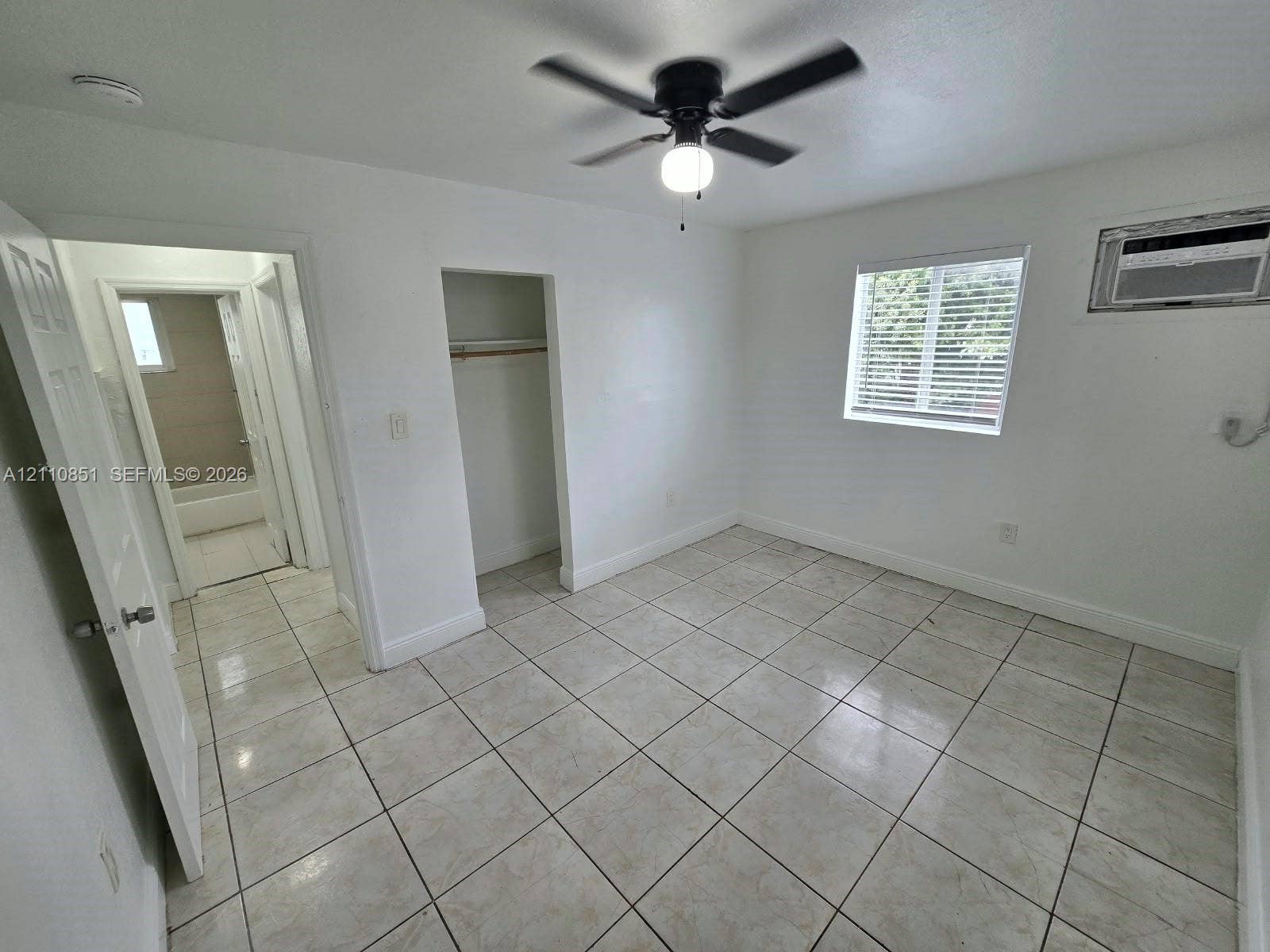 Room featuring neutral ceramic tile flooring, a ceiling-mounted light fixture with a fan, a window with integrated blinds, and an open closet