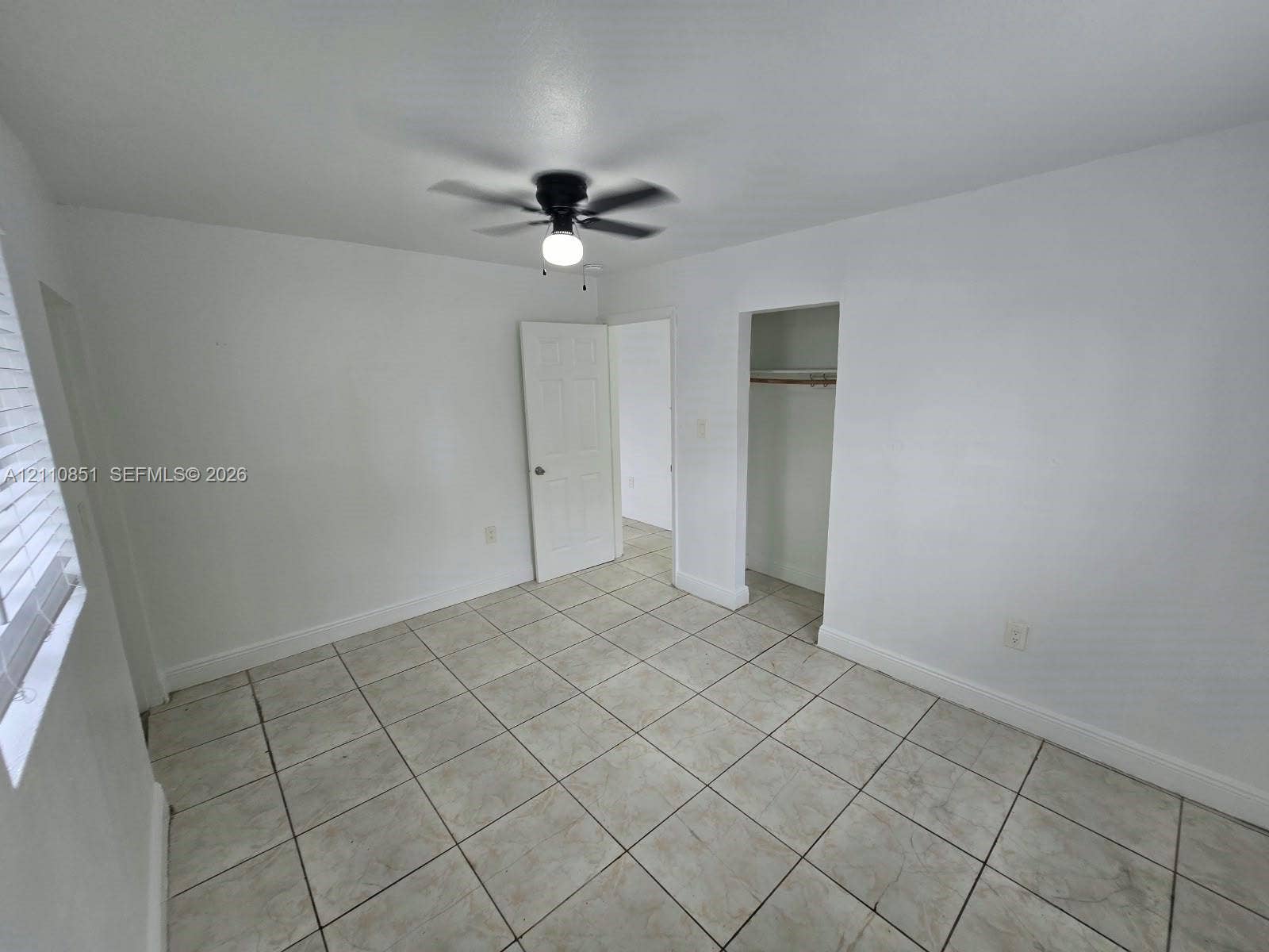 Ceramic tile flooring, white six-panel interior door, ceiling-mounted light fixture with fan, and a recessed closet space with a rod