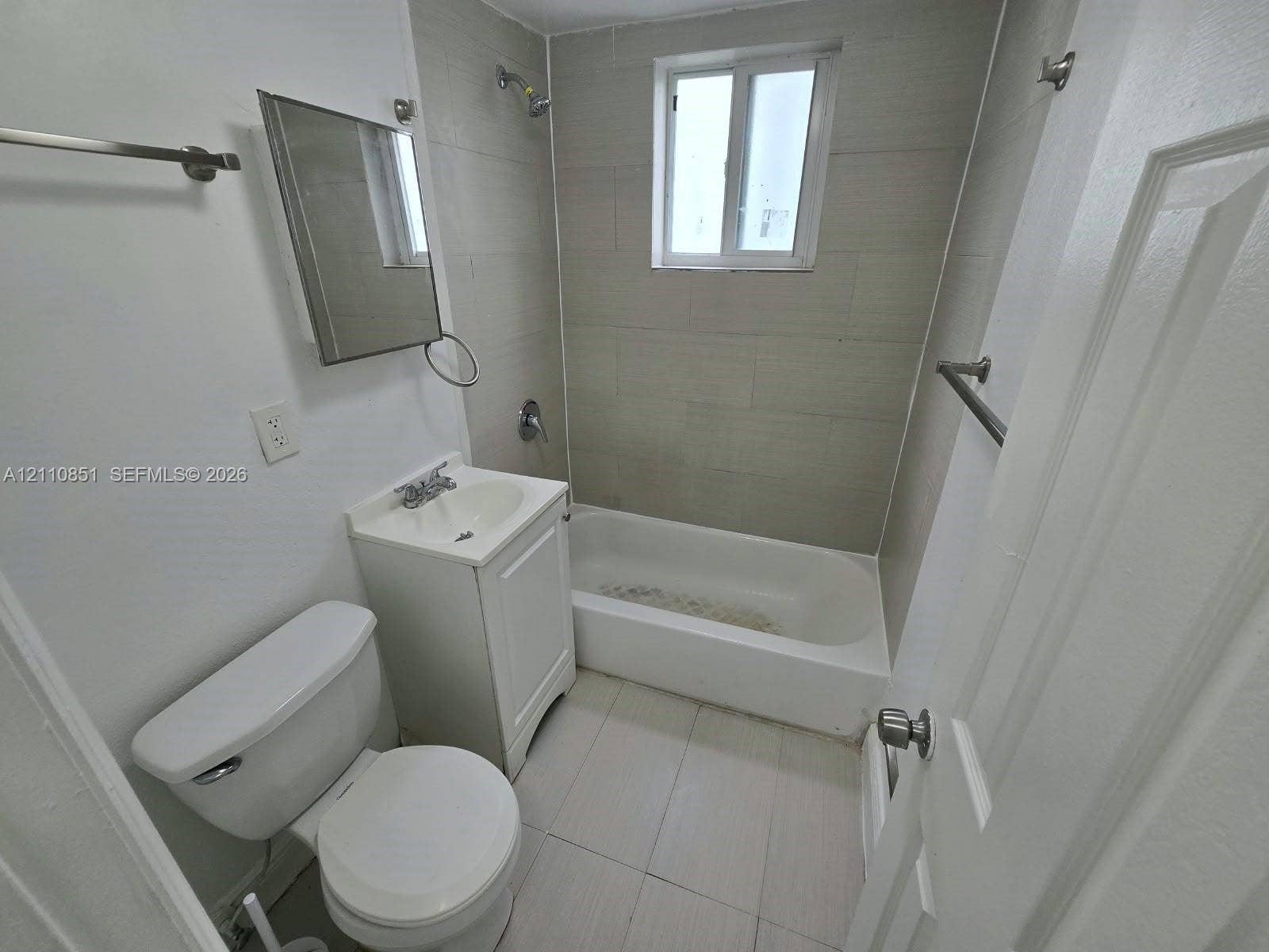 Bathroom featuring a white pedestal vanity, ceramic tile flooring, a tub-shower combination with tile surround, a rectangular wall-mounted mirror, and a single-pane window