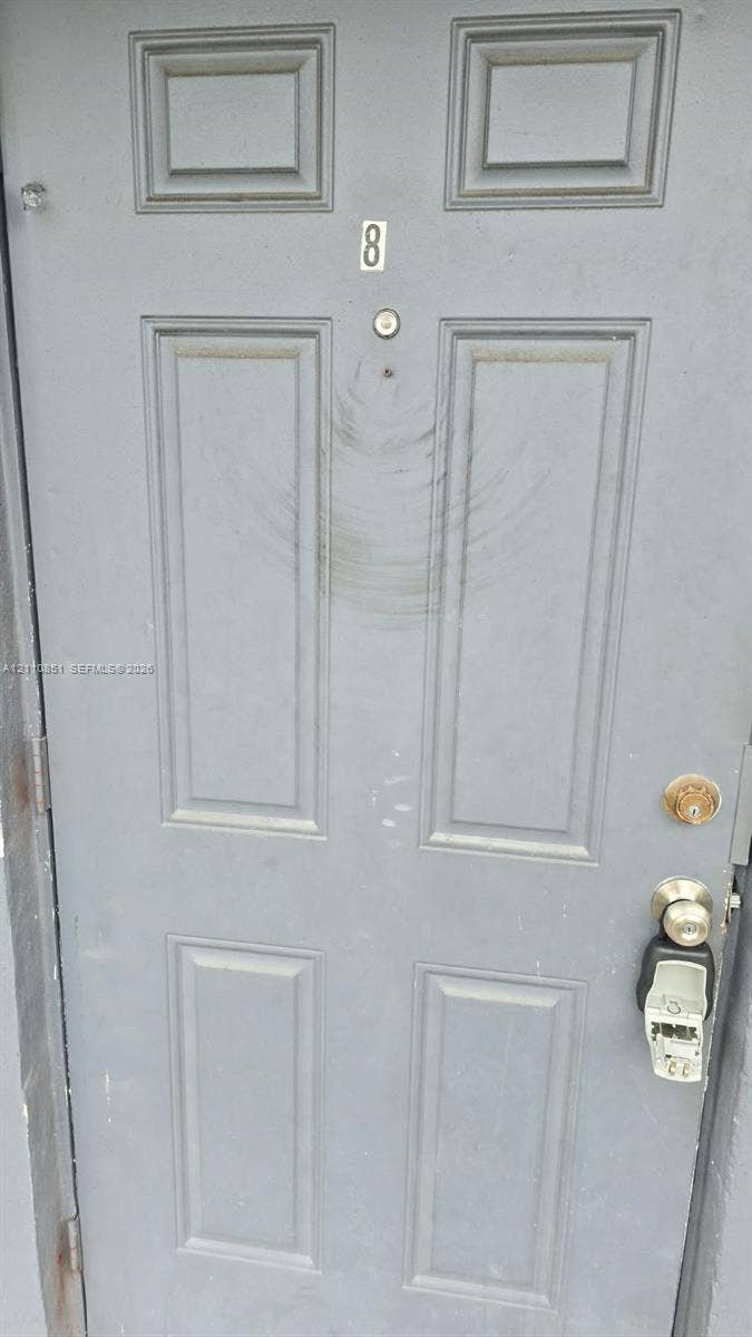 Grey-painted six-panel entry door featuring a brass-finished knob, deadbolt, and mounted door viewer