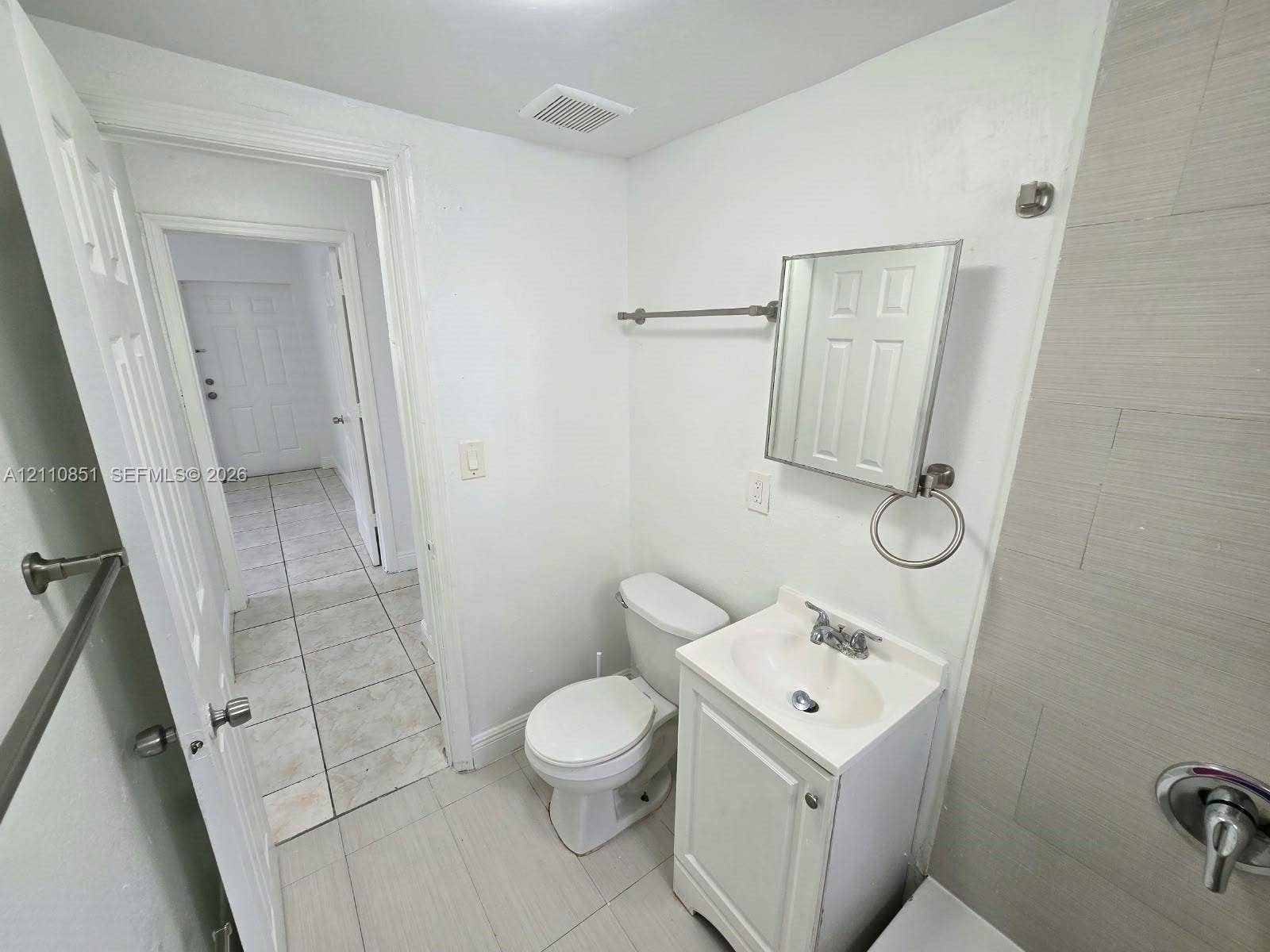 Bathroom featuring large-format tile flooring, a white vanity with an integrated basin, a mirrored medicine cabinet, and light-toned wall tile surrounding the shower area