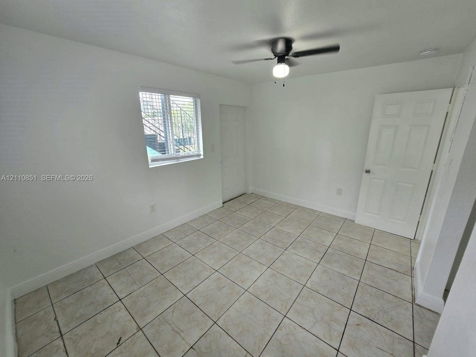 Interior room featuring neutral floor tiling, a multi-panel door, and a ceiling-mounted fan with integrated lighting
