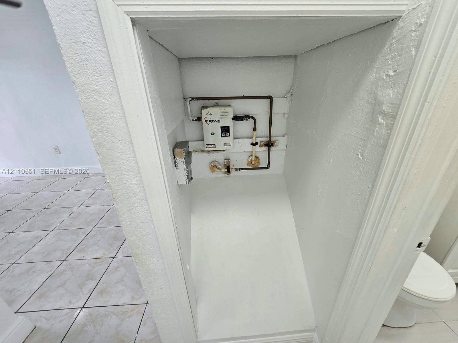 Recessed alcove featuring a wall-mounted tankless water heater, exposed copper piping, and white finished walls