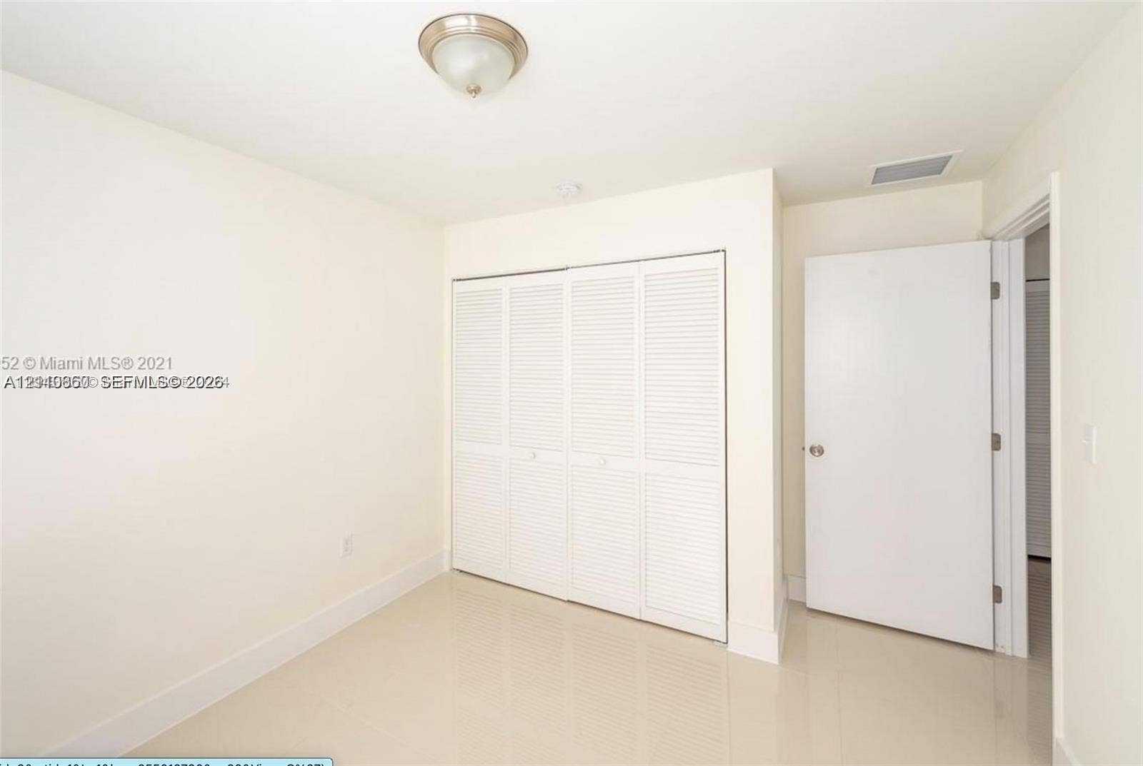 1530 NW 60th Street, Miami, FL 33142 Neutral-toned room featuring large-format tile flooring, a four-panel louvered closet, a semi-flush mount ceiling fixture, and a solid-core interior door
