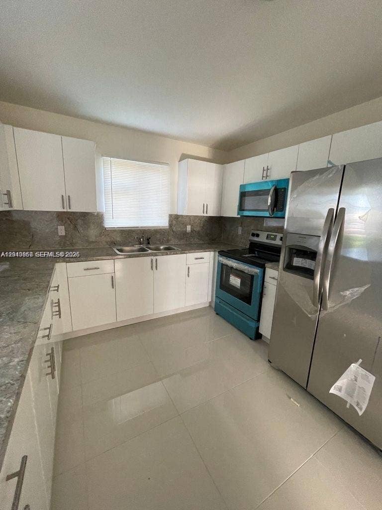 1530 NW 60th Street, Miami, FL 33142 Kitchen featuring white shaker-style cabinetry, stone-surface countertops, stone-tile backsplash, stainless steel appliances, and large-format tile flooring