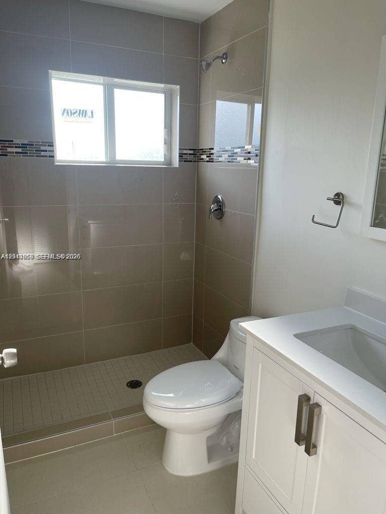 1530 NW 60th Street, Miami, FL 33142 Bathroom featuring a walk-in shower with large-format wall tile and decorative mosaic inlay, white vanity with integrated sink, and chrome fixtures