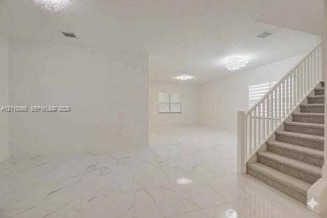 17552 SW 46th Street, Miramar, Miramar, FL 33029 Open-concept interior featuring large-format polished tile flooring, a staircase with white balusters and neutral carpeting, multi-tier crystalline chandeliers, and horizontal blind window treatments