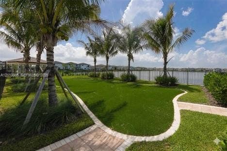 17552 SW 46th Street, Miramar, Miramar, FL 33029 Backyard featuring artificial turf, paver walkways, mature palm trees, a perimeter metal fence, and water frontage