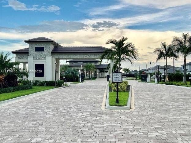 17552 SW 46th Street, Miramar, Miramar, FL 33029 Gated community entrance featuring a stone-clad guardhouse, tile roof, and paver driveway surrounded by mature palm trees and manicured landscaping
