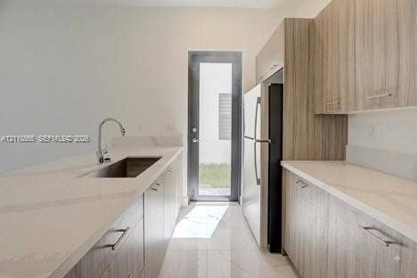17552 SW 46th Street, Miramar, Miramar, FL 33029 Kitchen featuring flat-panel wood-finish cabinetry, light-toned stone-finish countertops, stainless steel undermount sink with gooseneck faucet, full-height glass-panel exterior door, and polished tile flooring