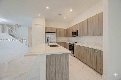 17552 SW 46th Street, Miramar, Miramar, FL 33029 Kitchen featuring flat-panel wood-finish cabinetry, stone-surface countertops, a center island with an integrated sink, stainless steel appliances, and large-format tile flooring