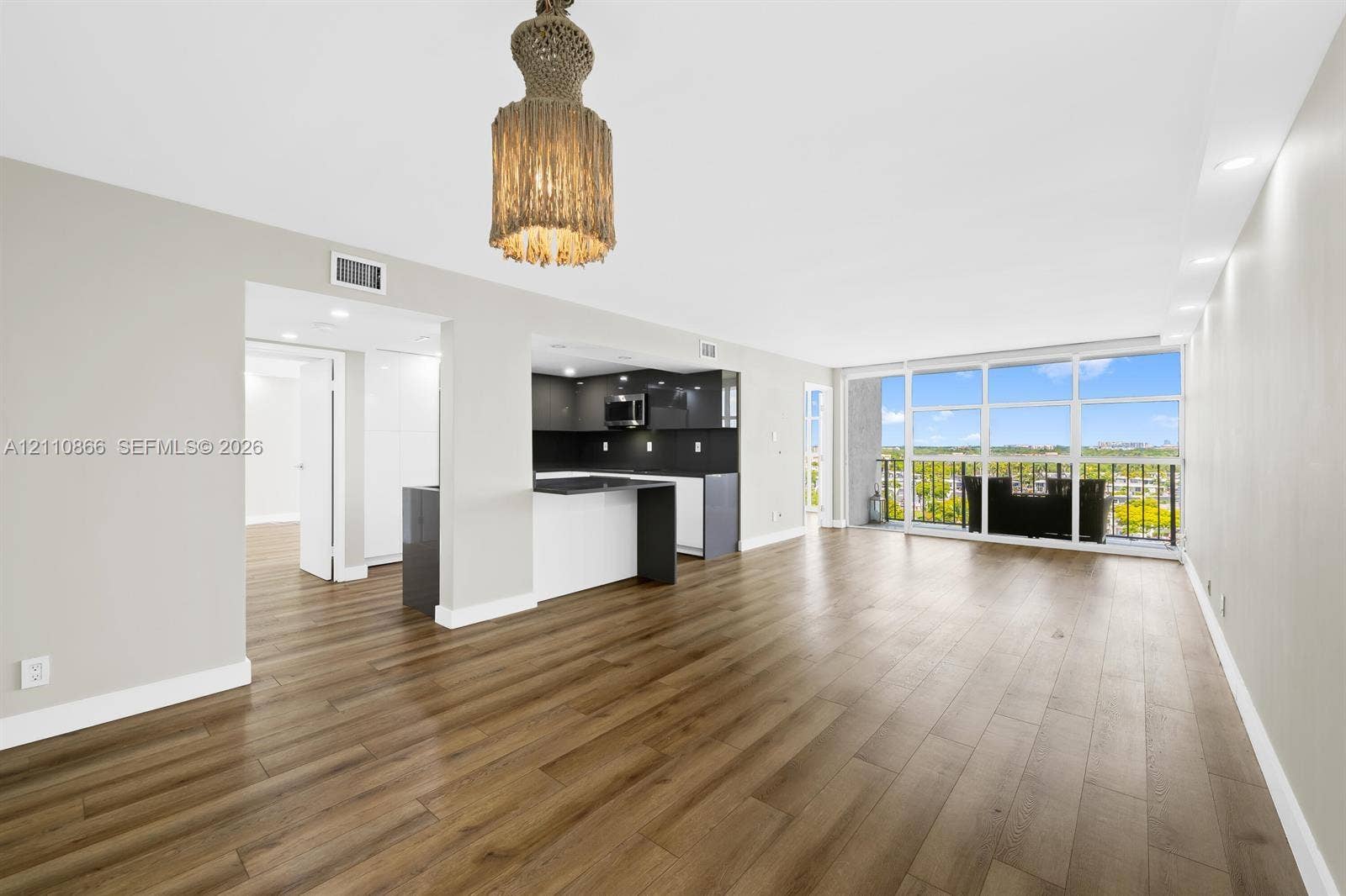 Open-concept space featuring wood-finish flooring, a kitchen with high-contrast cabinetry, recessed lighting, a statement pendant fixture, and floor-to-ceiling windows