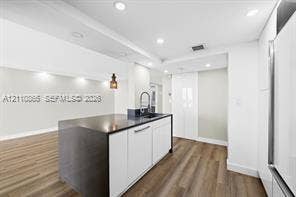 Kitchen featuring white flat-panel cabinetry, a dark-toned island with an integrated sink and gooseneck faucet, wood-finish flooring, and recessed ceiling lighting