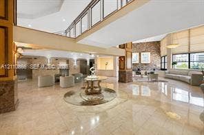Expansive lobby featuring polished stone flooring, a multi-story atrium with a mezzanine balcony, natural stone accent wall, and multiple stainless steel elevator access points