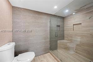 Walk-in shower featuring a frameless glass enclosure, recessed wall niche, and integrated bench seat, complemented by neutral-toned wall tiling and recessed lighting
