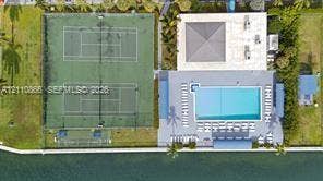 Aerial view featuring two tennis courts, a rectangular swimming pool, and concrete patio space situated on the water