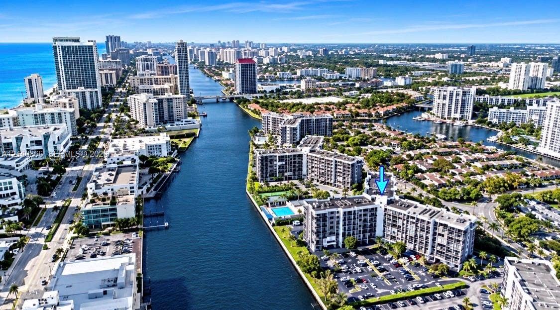 Aerial perspective of multi-story residential building featuring exterior balconies, surface parking, and waterfront positioning along an inland canal