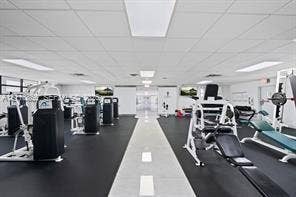 Fitness room featuring rubberized flooring, a center tile aisle, recessed fluorescent lighting, and wall-mounted televisions