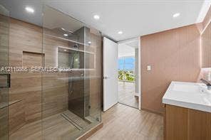 Walk-in shower with wood-finish tile surround, integrated shower niche, glass enclosure, and wood-finish cabinetry with a white countertop