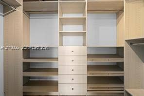 Custom-built closet system featuring light-toned finish cabinetry, adjustable shelving, integrated hanging rods, and a central stack of five soft-close drawers
