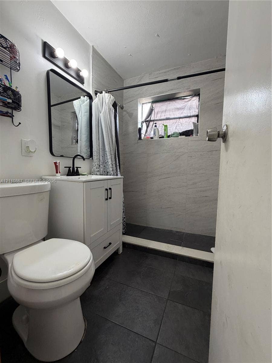 Bathroom featuring a white vanity cabinet, rectangular wall-mounted mirror, matte black fixtures, dark floor tile, and light-toned wall tile