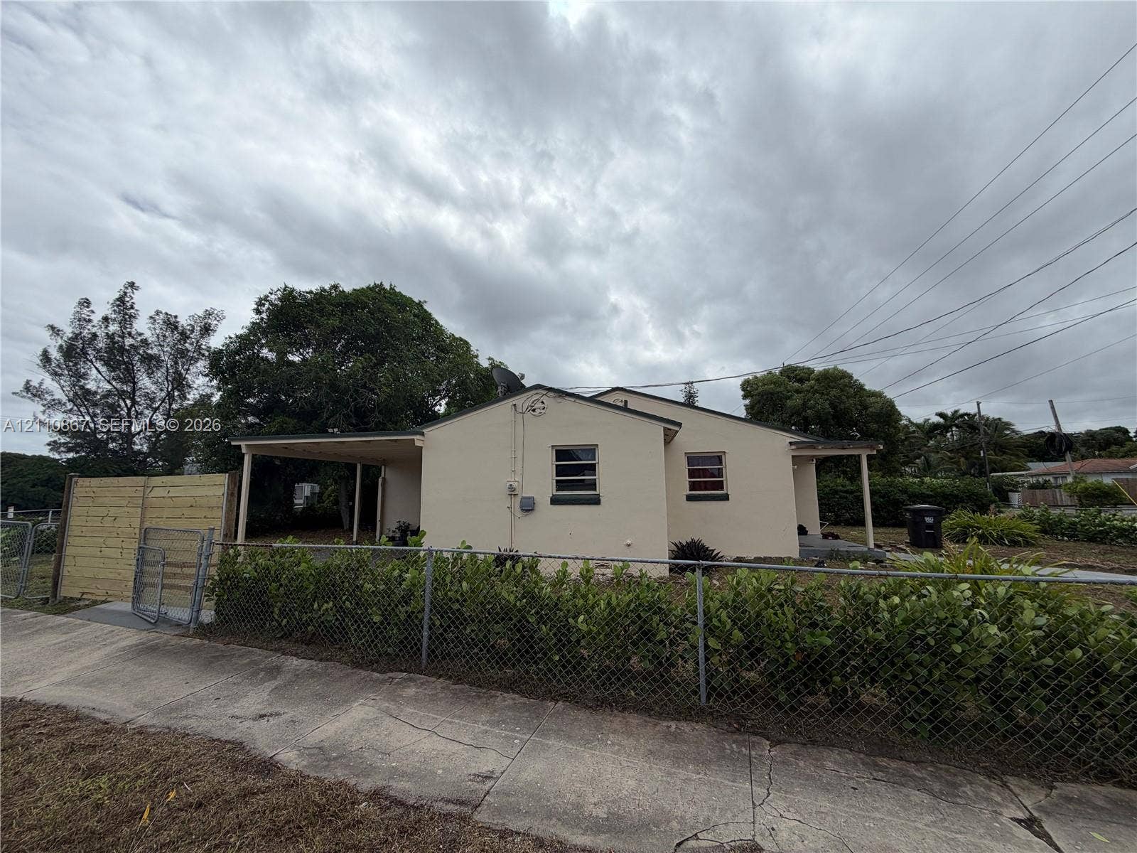 Stucco exterior featuring a covered carport, wood privacy fencing, chain-link perimeter fencing, and mature trees
