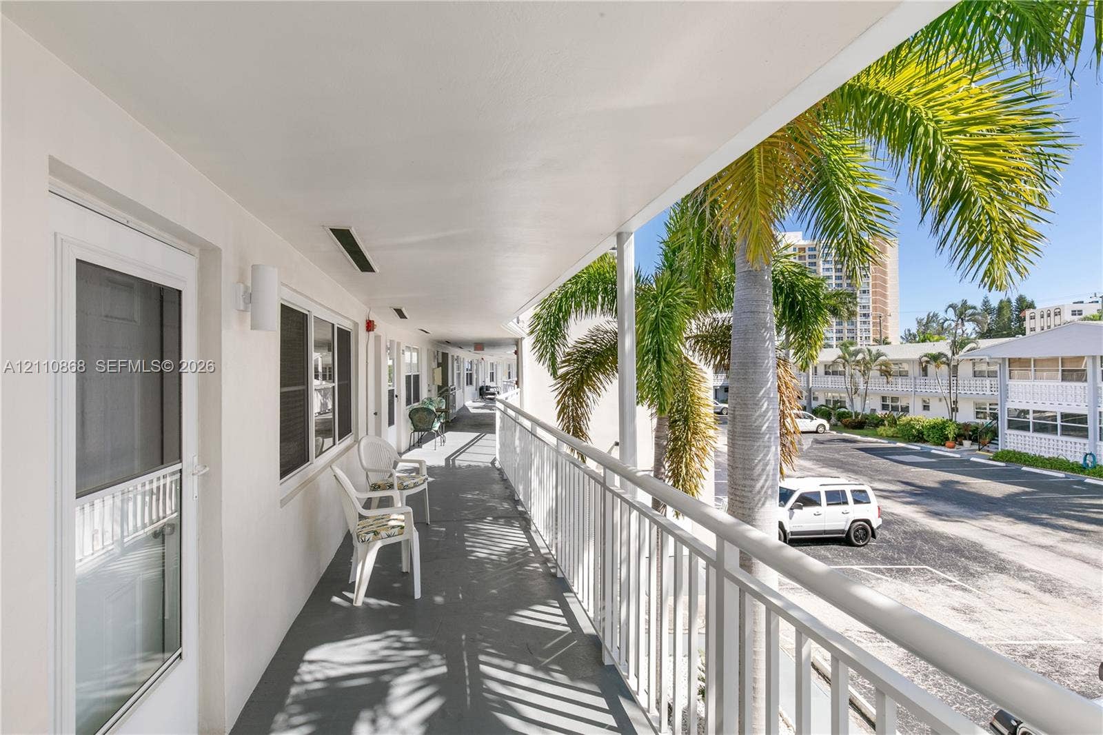 3121 S Ocean Drive, #209, Hallandale Beach, FL 33009 Covered exterior walkway featuring a white metal railing, wall-mounted light fixtures, and solid-surface flooring