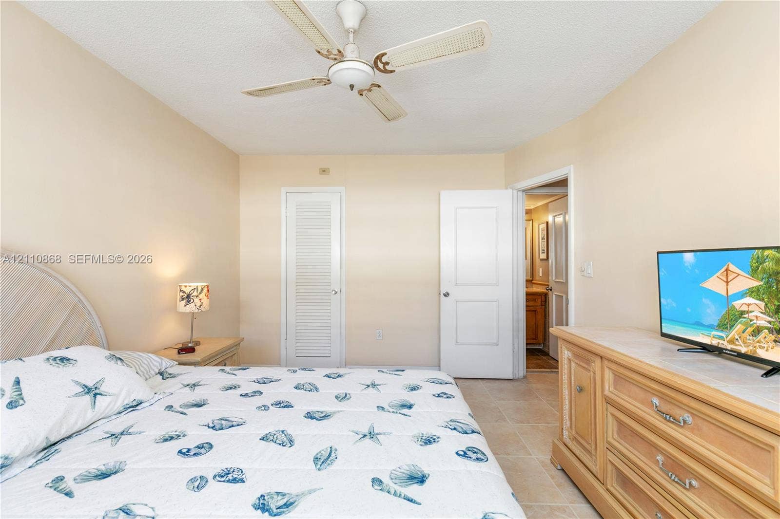 3121 S Ocean Drive, #209, Hallandale Beach, FL 33009 Interior room featuring neutral wall tones, large-format tile flooring, a white paneled door, a white louvered-style closet door, and a ceiling fan with integrated lighting