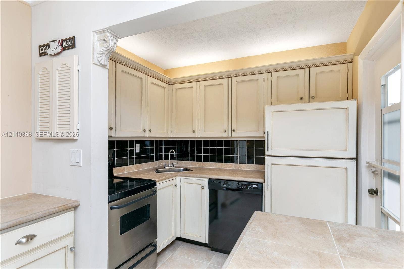 3121 S Ocean Drive, #209, Hallandale Beach, FL 33009 Kitchen featuring light-toned shaker cabinetry, black tiled backsplash, stone-finish countertops, and integrated stainless steel and black appliances