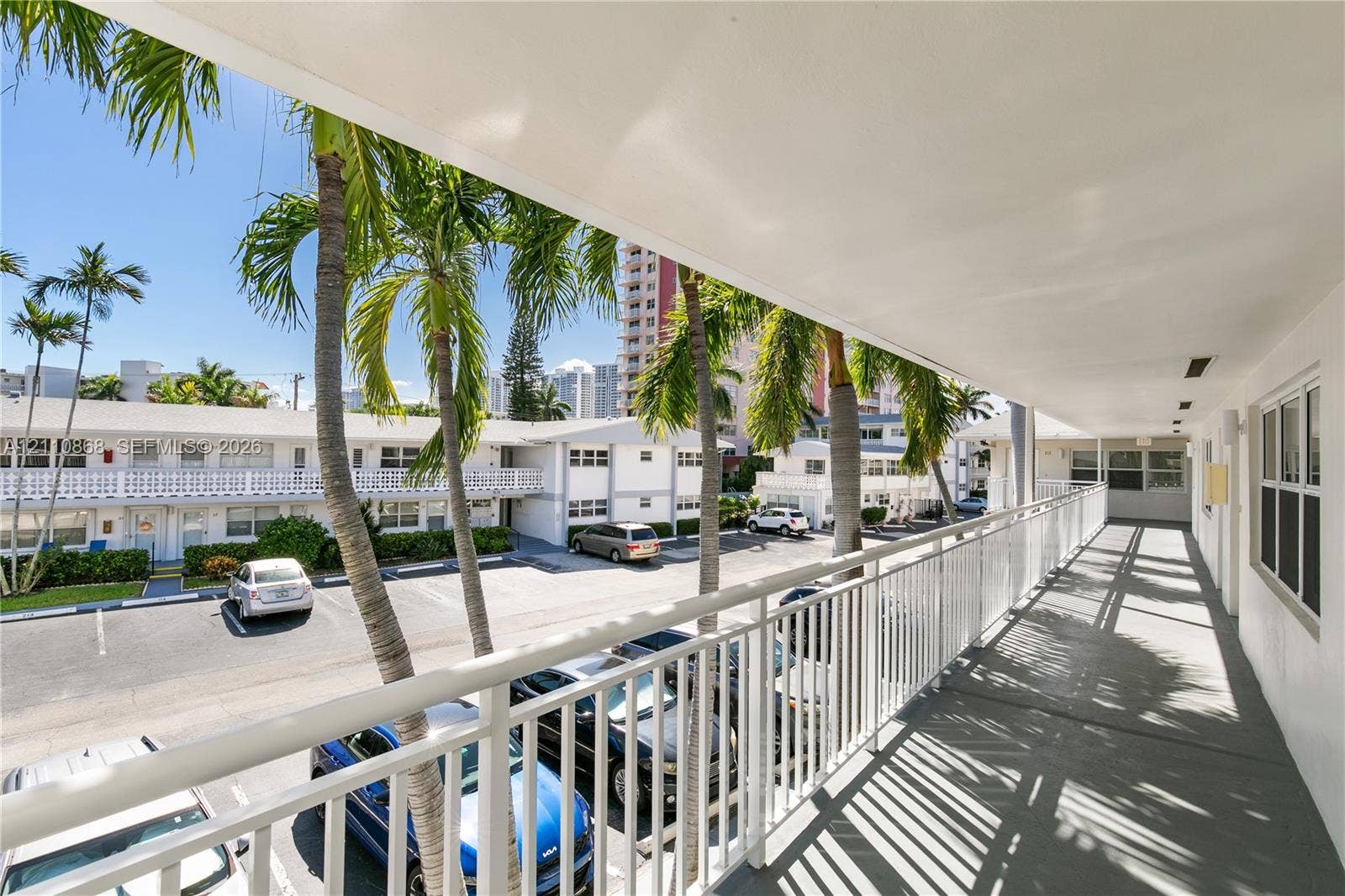 3121 S Ocean Drive, #209, Hallandale Beach, FL 33009 Covered exterior walkway featuring white metal railings, concrete flooring, and palm tree landscaping