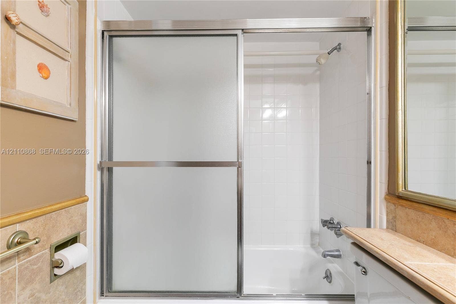 3121 S Ocean Drive, #209, Hallandale Beach, FL 33009 Shower with sliding frosted glass doors, white tile surround, metal shower head and faucet hardware, and light-toned tile wainscoting
