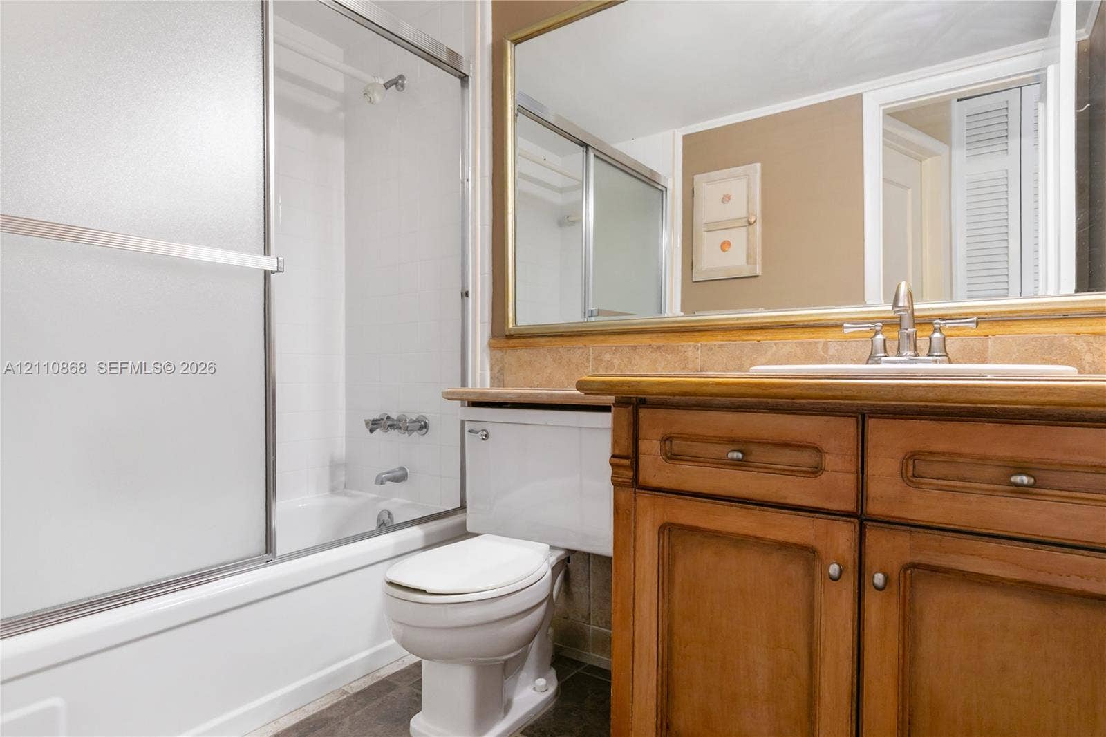 3121 S Ocean Drive, #209, Hallandale Beach, FL 33009 Bathroom featuring a wood vanity with integrated countertop, metal-framed wall mirror, and tub-shower combination with sliding glass doors